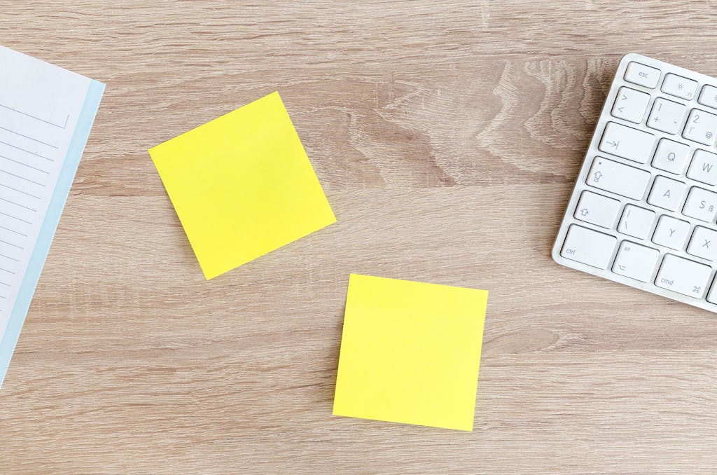 Flat lay of a workspace featuring yellow sticky notes, a keyboard, and a notebook on a wooden desk.