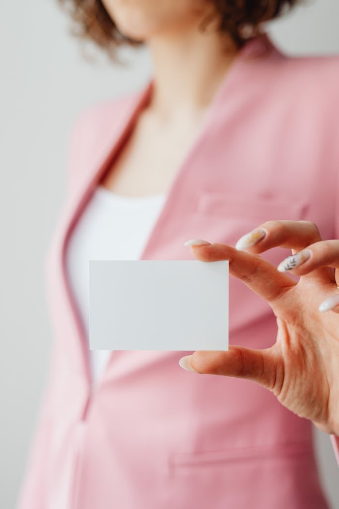 Close-up of a woman in a pink blazer holding a blank business card, ideal for mockups.